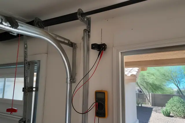 Garage door safety sensor and diagnostic equipment on a door track in a Phoenix, AZ workshop.