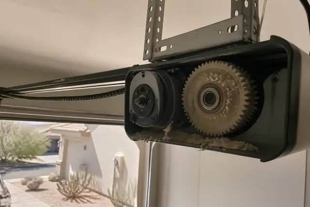 Shredded nylon gear debris and a sagging drive chain inside a garage door opener motor in Phoenix, AZ.