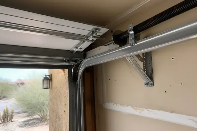 Garage door tracks, hinges, and reinforcement struts on a wall in Phoenix, AZ, with desert landscaping visible outside.