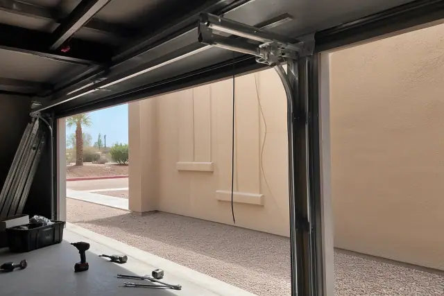 Technician repairing a commercial garage door track in a Phoenix, AZ warehouse with tools on the concrete floor.