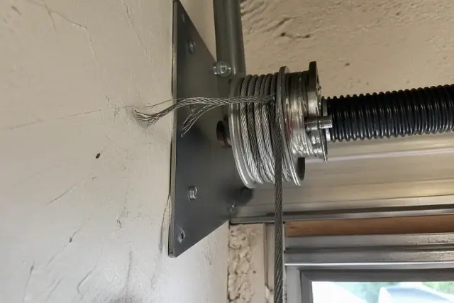 Frayed steel garage door cable unraveling near a metal drum mechanism in Phoenix, AZ.