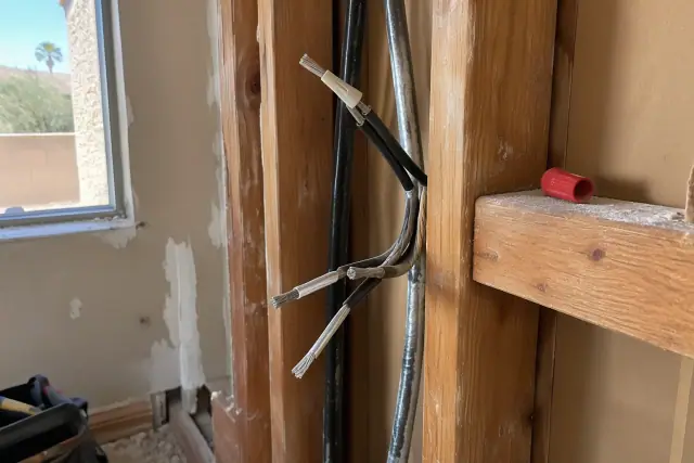 Contractor photo of old metal electrical cables being replaced in a wall in Gilbert, AZ.