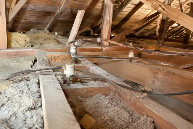 Attic access above walls for copper rewiring in Phoenix, AZ, showing vintage insulators and dusty wooden framing.