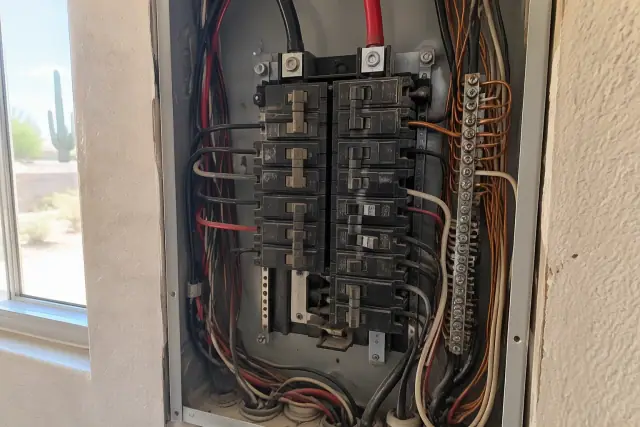 Electrician replacing a circuit breaker in an open electrical panel during a whole house rewiring in Chandler, AZ.