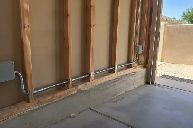 Armored electrical cable running along a masonry foundation for a dedicated circuit installation in Phoenix, AZ.