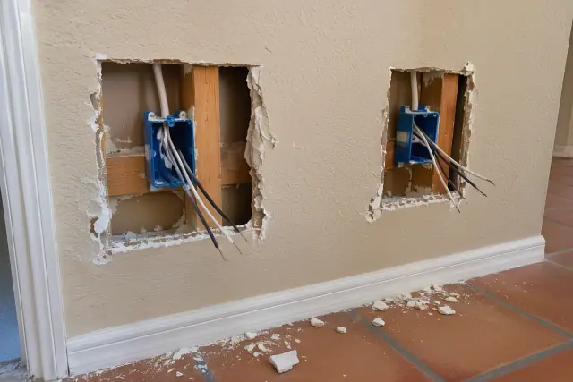 Drywall openings around outlet boxes with exposed wiring and studs during rewiring in Phoenix, AZ.
