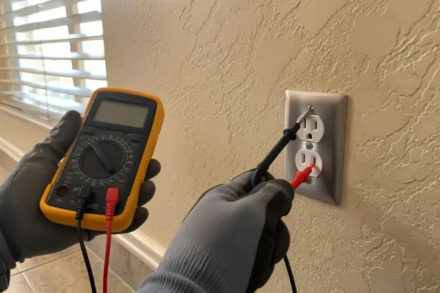 Technician testing a wall outlet with a digital multimeter during an electrical inspection in Phoenix, AZ.