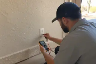 Technician testing a traditional duplex receptacle outlet with a digital multimeter in Phoenix, AZ.