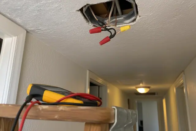 Digital multimeter near an open ceiling junction box during electrical troubleshooting in Glendale, AZ.