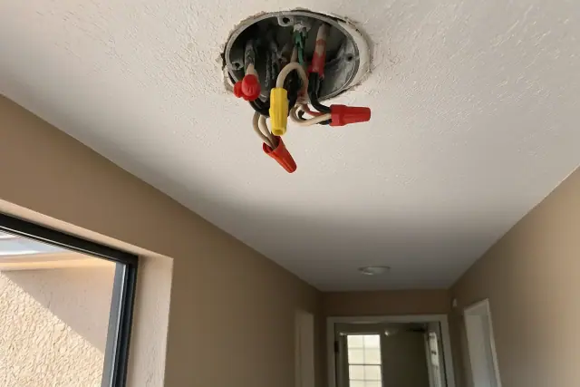 Technician photographing an open ceiling junction box with exposed wires during rewiring in Mesa, AZ.