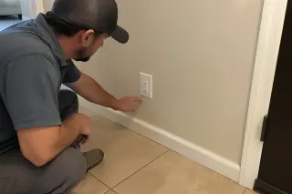 Service professional inspecting a completed electrical outlet installation with beige ceramic tile flooring in Phoenix, AZ.