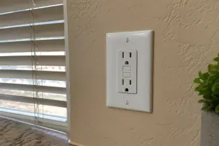 Completed GFCI safety outlet and wall plate on a stucco interior wall in Phoenix, AZ.