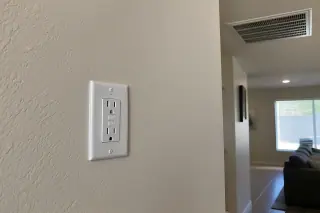 Finished white GFCI outlet plate flush on a stucco interior wall in Phoenix, AZ.