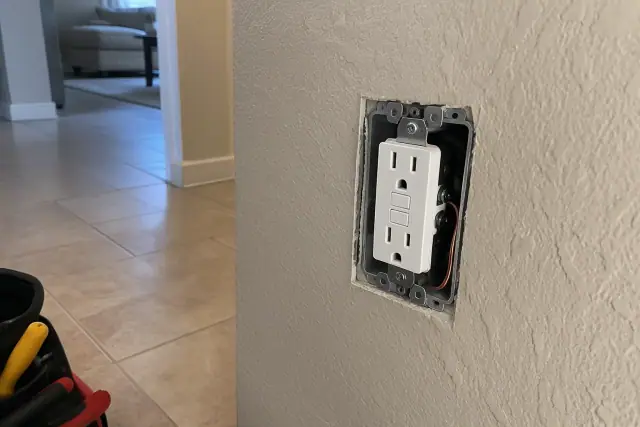 GFCI outlet installation on a stucco wall with a visible grounding wire in Phoenix, AZ.