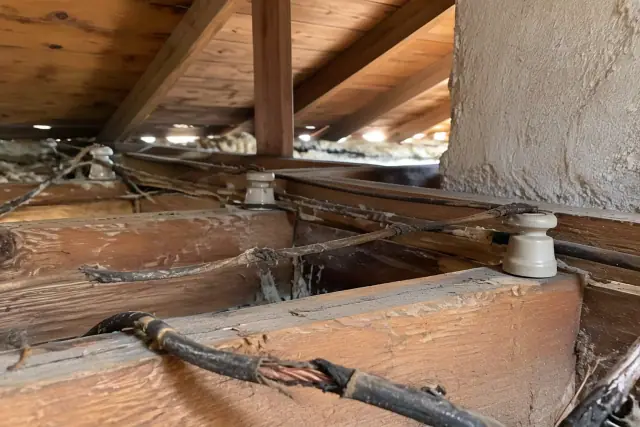 Knob and tube wiring replacement in a Mesa, AZ attic with vintage ceramic insulators and timber framing.