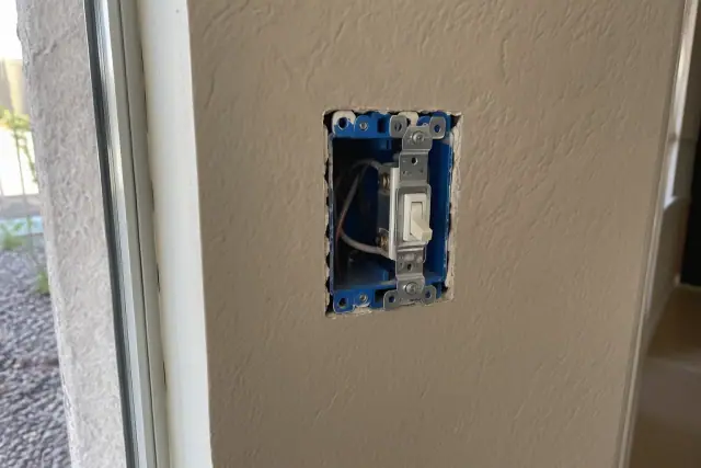 Drywall cutout showing an electrical box and wires during whole house rewiring in Mesa, AZ.