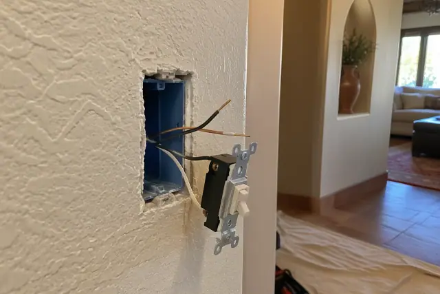 Drywall cutout showing an electrical box and wires for switch installation in Gilbert, AZ.