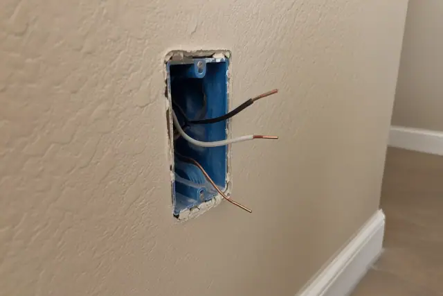 Drywall cutout with a plastic electrical box and stripped copper wires in Goodyear, AZ.
