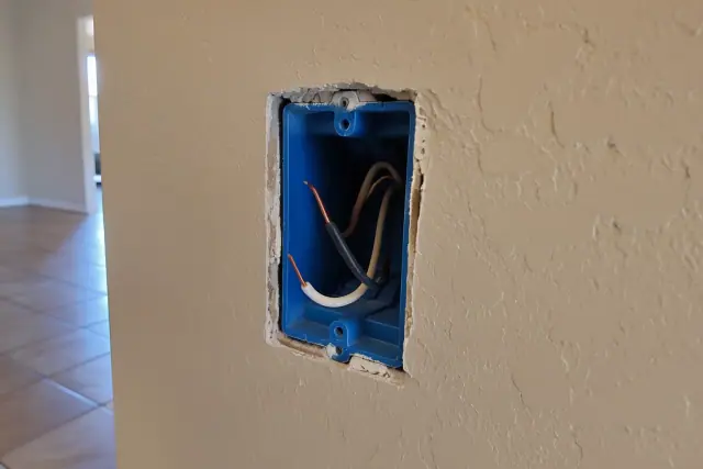 Drywall cutout with stripped copper wires in a plastic electrical box during whole house rewiring in Chandler, AZ.
