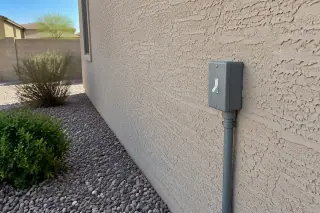 Completed electrical switch installation on an exterior stucco wall with desert gravel in Phoenix, AZ.