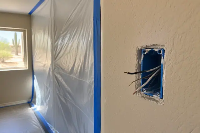 Plastic dust barrier taped over a drywall cutout with exposed wires in a Phoenix, AZ home.
