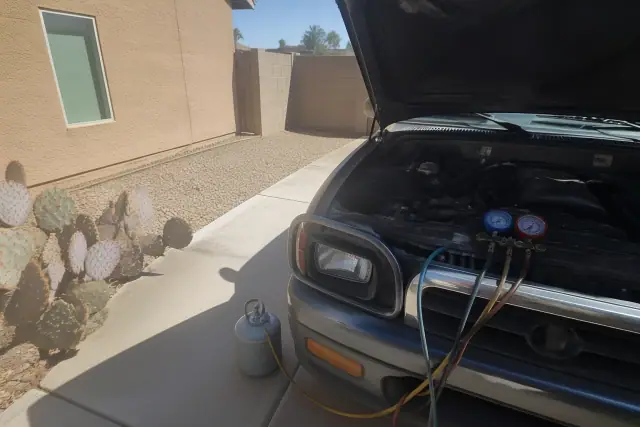 Manifold gauges connected to an engine with an open hood for AC repair at a residential home in Peoria, AZ.