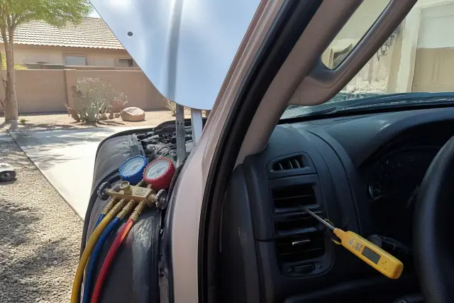 Mechanic performing an AC repair and recharge on a car in a driveway in Gilbert, AZ.