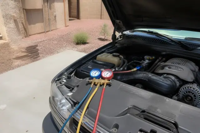 Technician checking car AC system with pressure gauges in a residential driveway in Glendale, AZ.