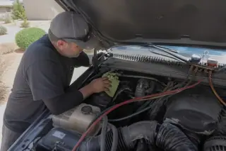 Technician wiping an engine bay with a microfiber cloth near AC service ports in a Phoenix, AZ driveway.