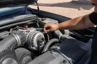 Technician checking battery terminal connections on an alternator in a Phoenix, AZ driveway.