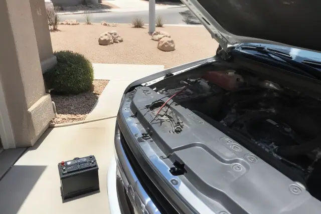 Technician replacing a car battery under the hood of a vehicle on a driveway in Phoenix, AZ.