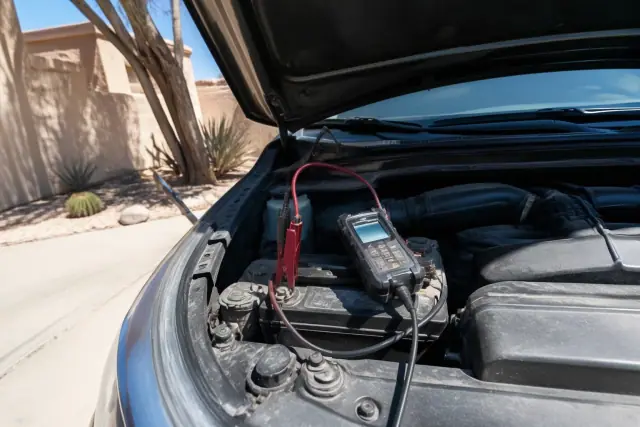 A technician performing a car battery health check on a vehicle in a driveway in Phoenix, AZ.