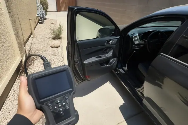Technician using a handheld diagnostic scanner on a vehicle in a Phoenix, AZ utility area.