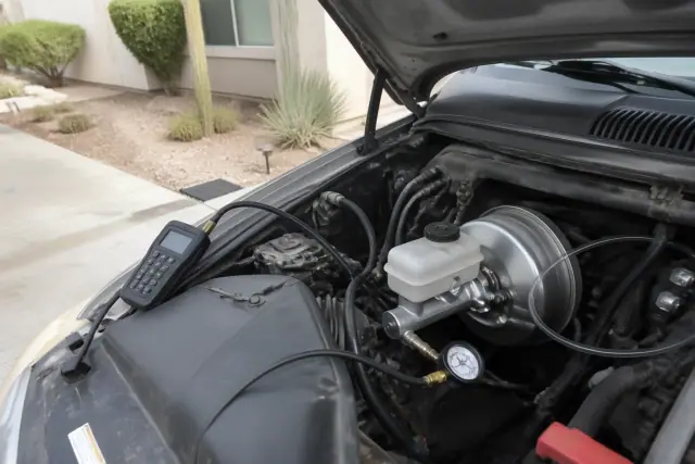 Technician diagnosing a brake master cylinder and booster in an engine bay at a home in Phoenix, AZ.