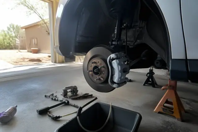 A car on jack stands undergoing brake caliper replacement in a residential garage in Phoenix, AZ.