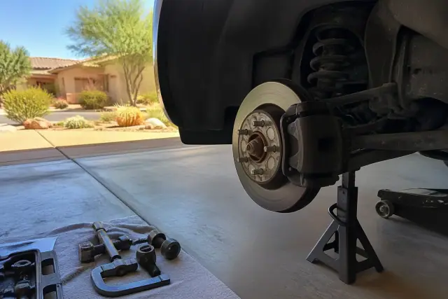 Vehicle on jack stands with brake tools in a Phoenix, AZ garage with desert landscaping visible in the background.