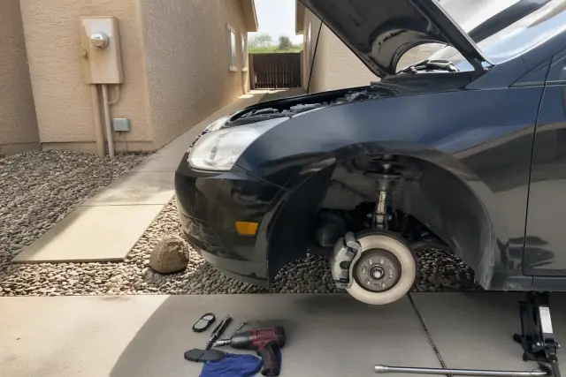 Technician performing a brake repair on a vehicle parked on a residential concrete pad in Avondale, AZ.