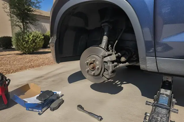 Mobile mechanic working on car brakes with the wheel removed on a concrete pad in Gilbert, AZ.