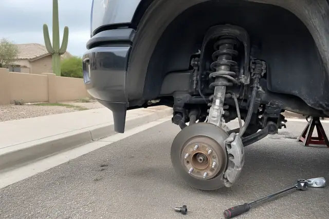Mechanic performing a brake and suspension inspection on a car on a residential street in Phoenix, AZ.