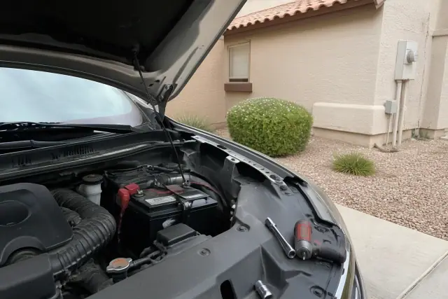 Mobile mechanic replacing a car battery on a vehicle in a residential driveway in Mesa, AZ.