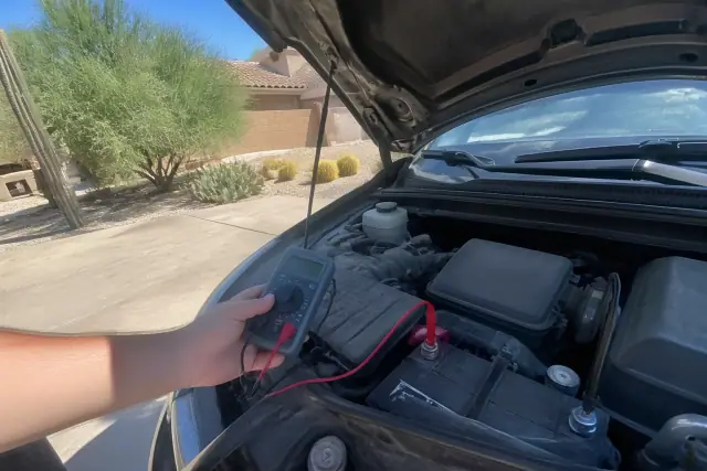 Technician using a multimeter to test a car battery on a driveway in Phoenix, AZ.