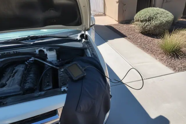 A mechanic performing check engine light diagnostics on a car in a residential driveway in Goodyear, AZ.