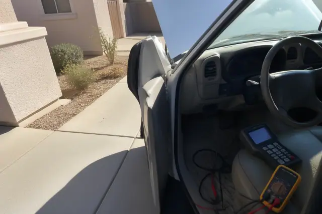 Diagnostic scanner and cables connected to a car under the dashboard in a Peoria, AZ driveway.