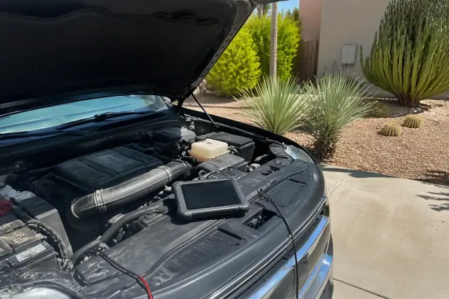 Diagnostic tablet plugged into an open vehicle engine bay for repairs at a home in Tempe, AZ.