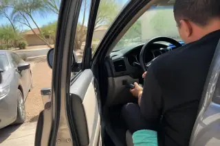 Technician using a diagnostic scanner on a car dashboard in a Phoenix, AZ driveway with desert landscaping.