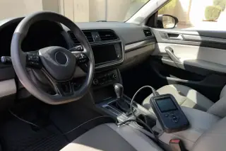 Handheld diagnostic scanner connected to a vehicle dashboard in a sunny driveway in Phoenix, AZ.