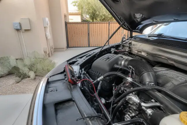 Technician inspecting alternator wiring with a multimeter on a vehicle in a Phoenix, AZ driveway.