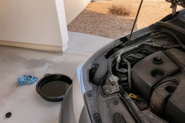 A vehicle with an open oil cap and a drain pan on a concrete pad at a home in Phoenix, AZ.