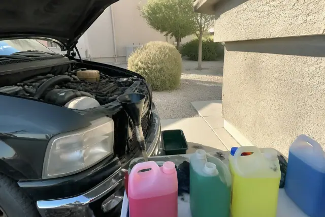 Car engine with coolant jugs, funnel, and drip tray on a concrete pad at a Phoenix, AZ home.