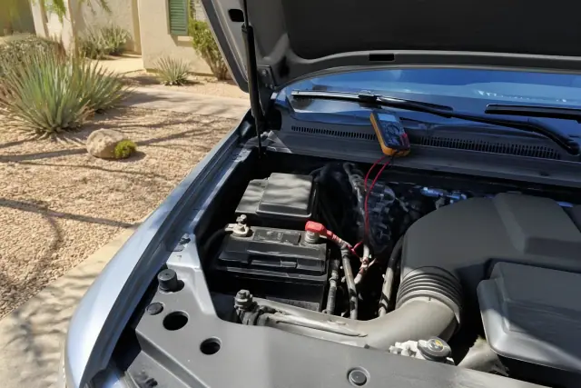 Car battery replacement with new terminals and a diagnostic tool under the hood of a car in a Phoenix, AZ driveway.